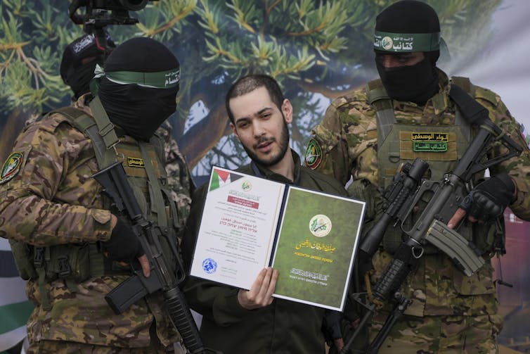 Um refém israelense flanqueado em ambos os lados por militantes mascarados do Hamas.
